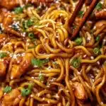 Plate of sticky garlic chicken noodles garnished with green onions