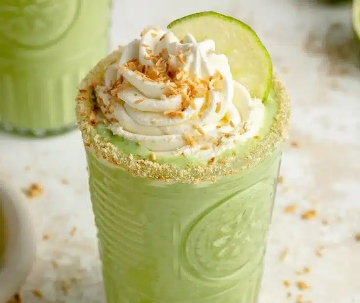 Creamy coconut key lime pie smoothie in a glass with lime wedges and coconut flakes
