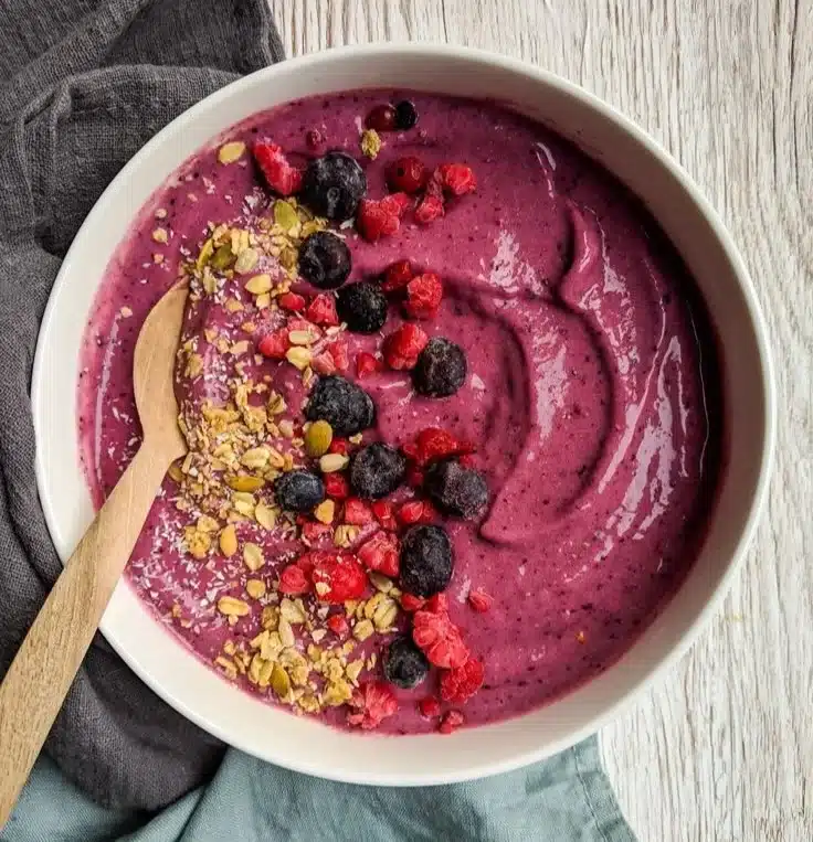 Colorful frozen fruit smoothie bowl topped with fresh fruits and granola