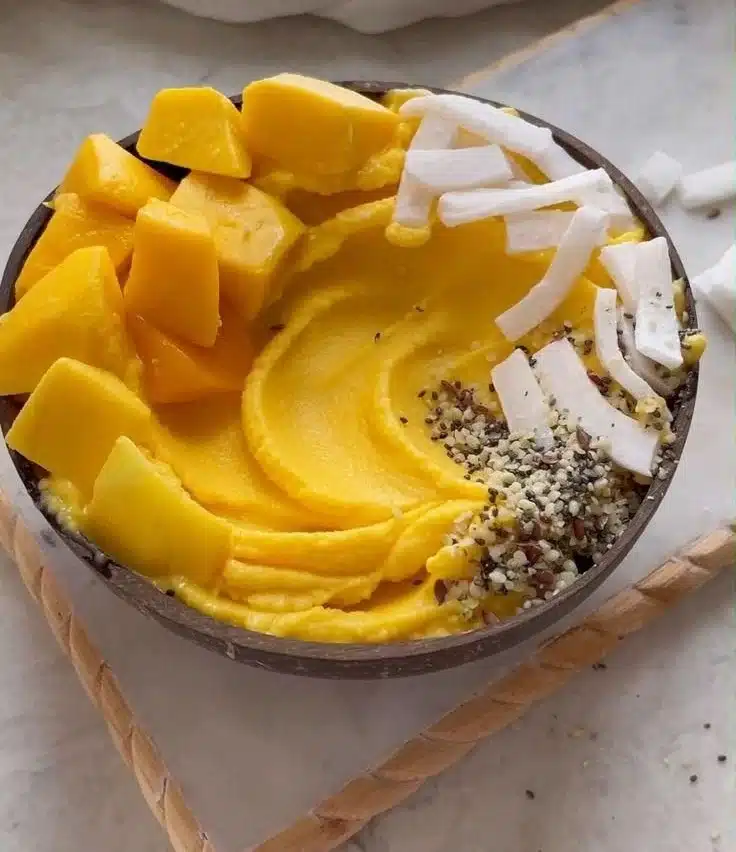 Delicious banana mango yogurt smoothie bowl topped with fresh fruits and seeds