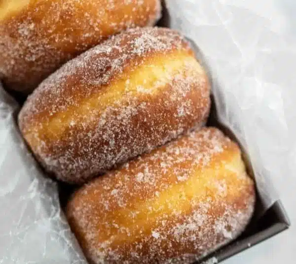 Freshly baked simple sugar donuts coated in sugar on a white plate