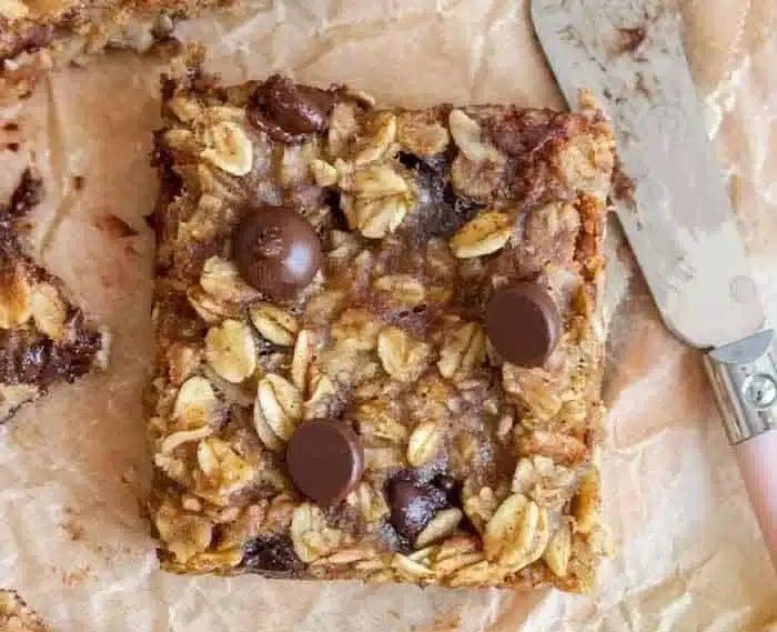 Homemade Banana Oatmeal Bars on a wooden table surrounded by bananas and oats
