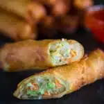 Golden fried spring rolls served with dipping sauce on a plate.