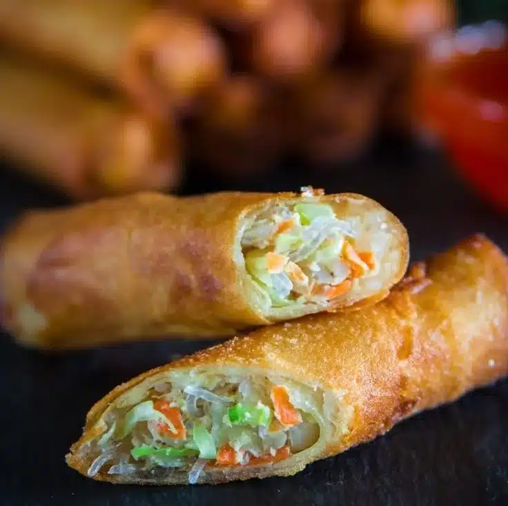 Golden fried spring rolls served with dipping sauce on a plate.