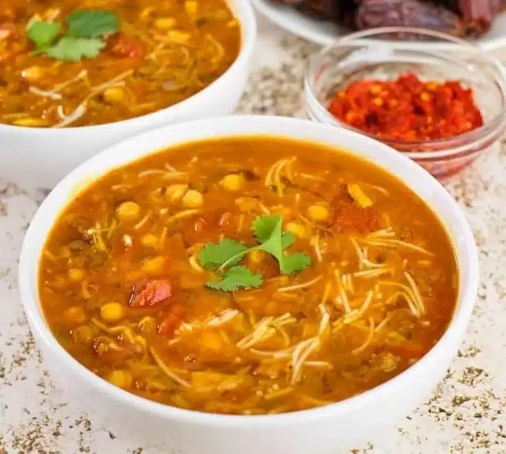 A bowl of steaming Harira, traditional Moroccan soup with spices and herbs.
