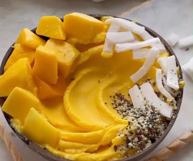 Thick mango smoothie bowl topped with fruits and seeds, no banana included